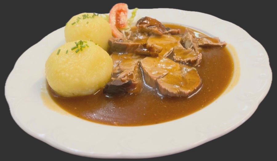 Teller mit Schweinebraten in dunkler Soße und zwei Klößen